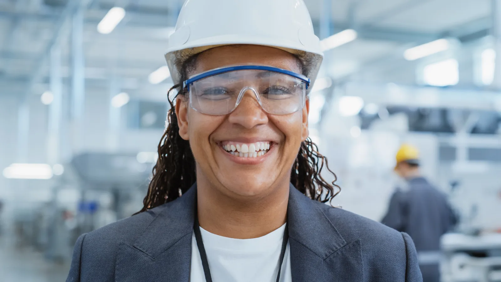 Safety professional wearing a white hard hat and clear protective glasses in a factory.