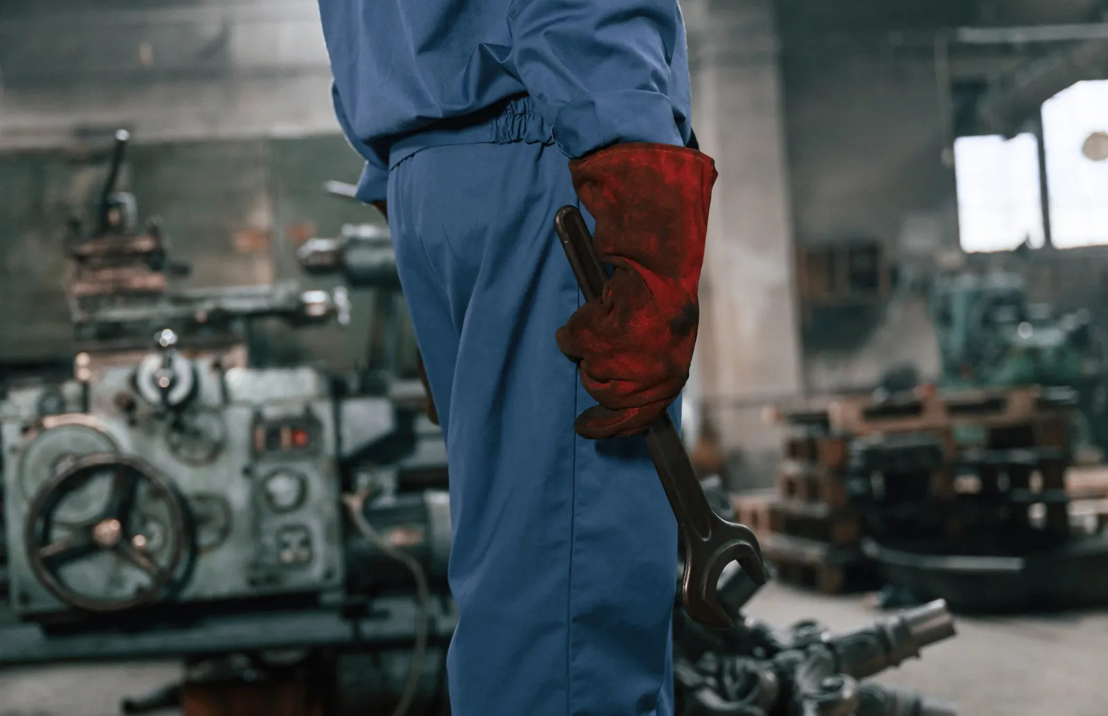 Workshop worker in blue overalls and protective gloves holding a large spanner.