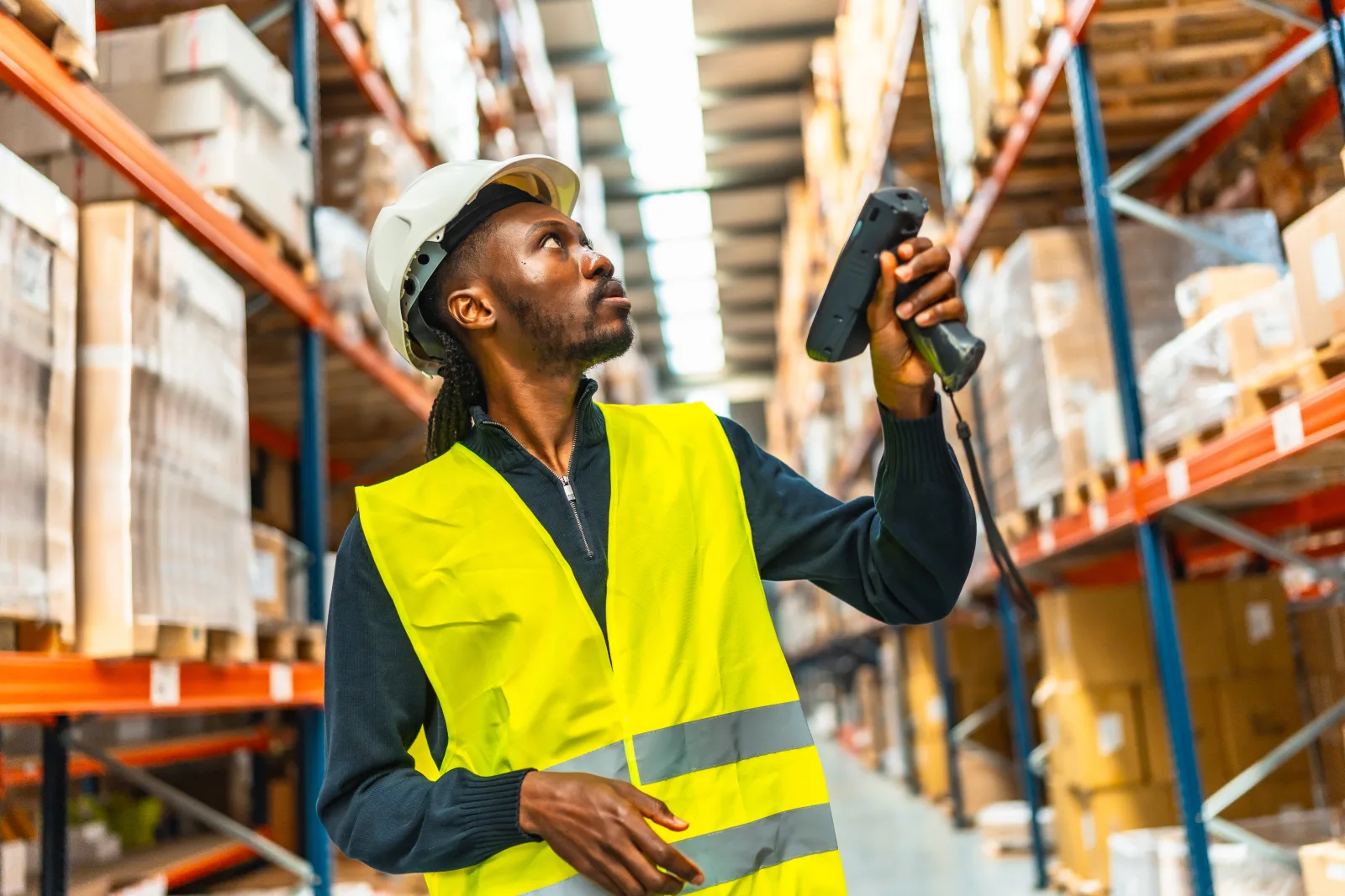 Warehouse worker in high-visibility clothing scanning stock on storage racks.